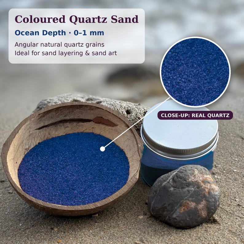 Op de afbeelding: Gekleurd kwartszand met het label Ocean Depth 0-1 mm, bestaande uit hoekige natuurlijke kwartskorrels in een diepblauwe kleur. Het zand zit in een bruine kokosnootschaal naast een pot met zilverkleurig deksel en een donkere steen.