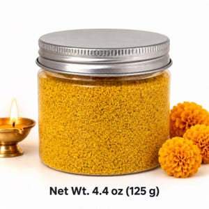 Closed clear jar of bright yellow colored quartz sand with a silver metal screw lid, next to a lit brass oil lamp and orange marigold flowers, with text: Net Wt. 4.4 oz (125 g).
