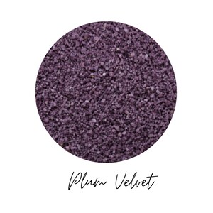 Close-up circle of Plum Velvet colored quartz sand showing fine plum purple grains, with the color name Plum Velvet written in script below, on a white background
