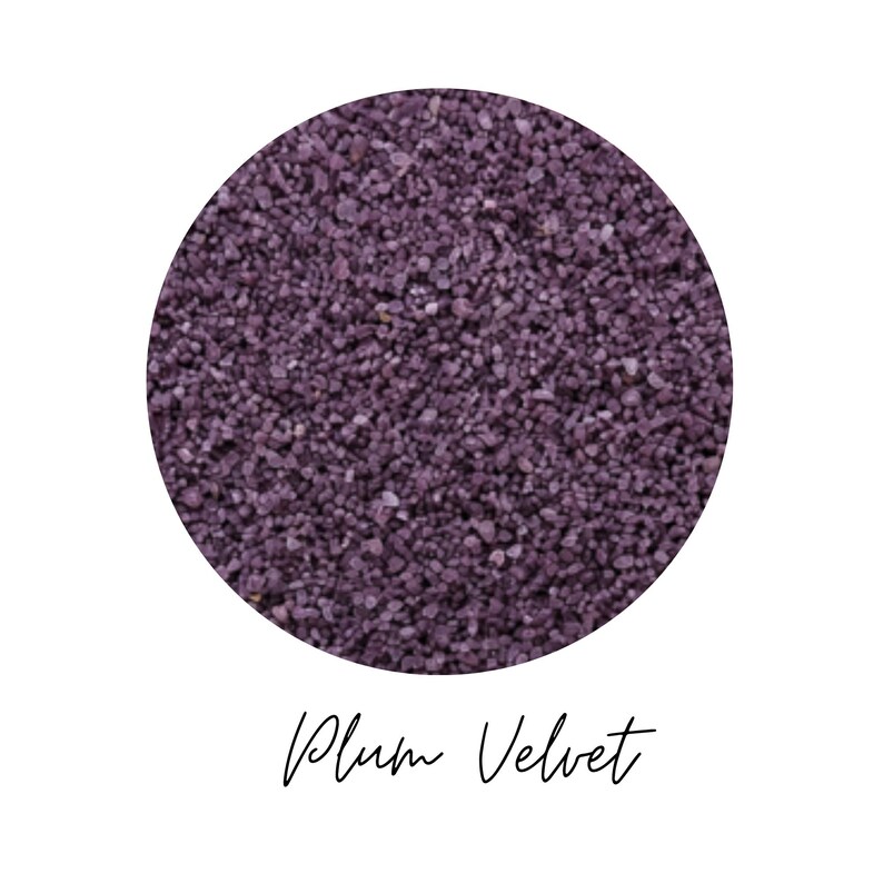 Close-up circle of Plum Velvet colored quartz sand showing fine plum purple grains, with the color name Plum Velvet written in script below, on a white background