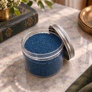 Open jar of Blue Lagoon colored quartz sand styled with a vintage book and gold home decor