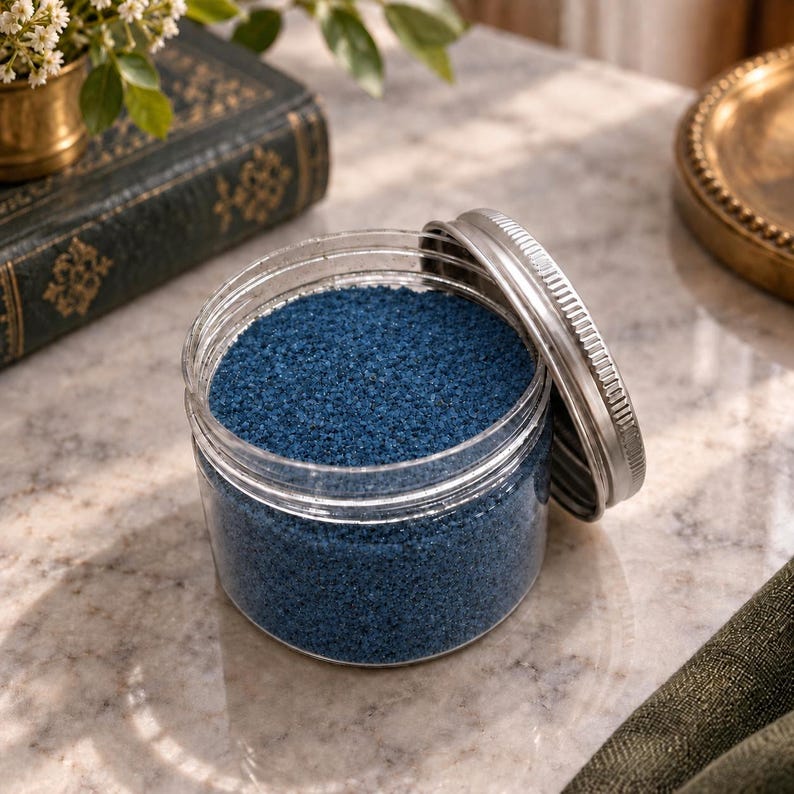 Open jar of Blue Lagoon colored quartz sand styled with a vintage book and gold home decor