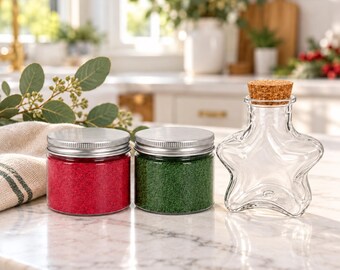 May include: Two cylindrical glass jars with silver metal lids, one filled with red granular material and one with green granular material, alongside a clear glass star-shaped bottle topped with a cylindrical cork stopper.