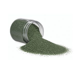 Clear jar tipped on its side with dark green craft sand spilling out onto a white surface