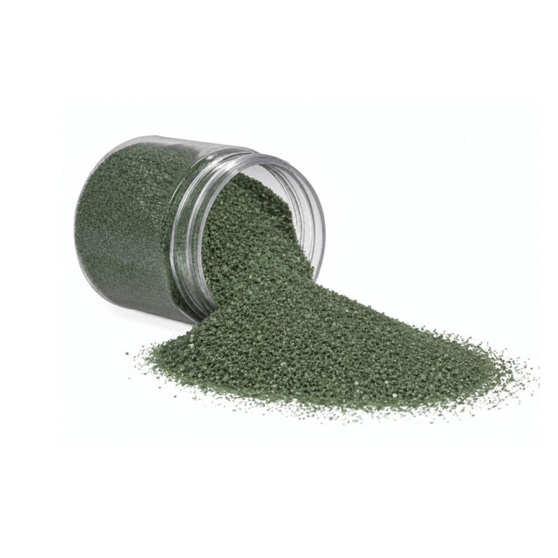 Clear jar tipped on its side with dark green craft sand spilling out onto a white surface