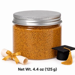 Closed clear jar of golden amber colored quartz sand with a silver metal screw lid, next to a rolled diploma tied with a gold ribbon and a black graduation cap with a gold tassel, with text: Net Wt. 4.4 oz (125 g).