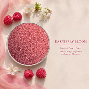 Round tin of Raspberry Bloom colored quartz sand on a cream background, surrounded by fresh raspberries, white blossoms and pink fabric, with text: Raspberry Bloom, Colored Quartz Sand, inspired by ripe raspberries and summer blossoms.