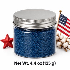 Closed clear jar of royal blue colored quartz sand with a silver metal screw lid, next to a red star, a small American flag and cotton stems, with text: Net Wt. 4.4 oz (125 g).