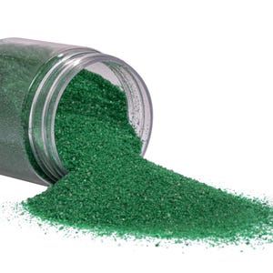 Clear jar tipped on its side with emerald green craft sand spilling out onto a white surface