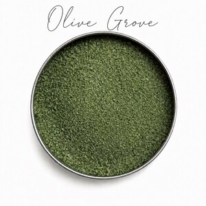 Top view of a round tin filled with Olive Grove olive green quartz sand, with the color name Olive Grove written in script above, on a white background