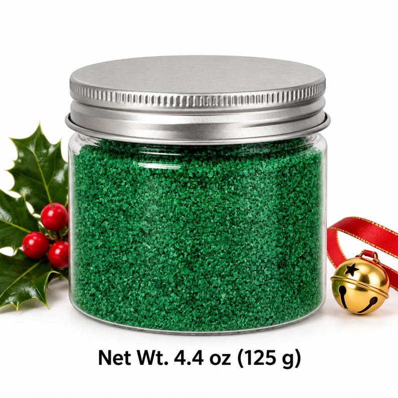Closed clear jar of bright green colored quartz sand with a silver metal screw lid, next to holly leaves with red berries and a gold jingle bell on a red ribbon, with text: Net Wt. 4.4 oz (125 g).