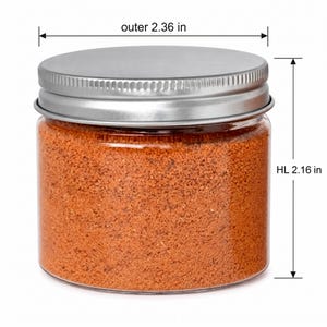 Closed clear jar of warm orange colored quartz sand with a silver metal screw lid, with measurement lines showing an outer diameter of 2.36 in (6 cm) and a height of 2.16 in (5.5 cm), on a white background.