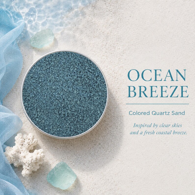 Round tin of Ocean Breeze colored quartz sand on white beach sand, surrounded by light blue fabric, sea glass and white coral, with text: Ocean Breeze, Colored Quartz Sand, inspired by clear skies and a fresh coastal breeze