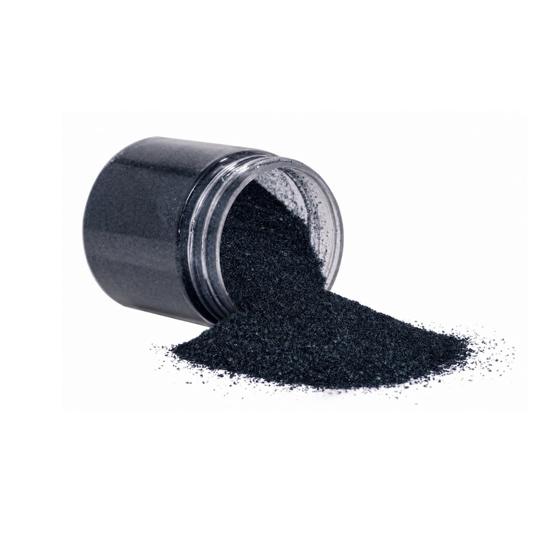 Clear jar tipped on its side with dark navy craft sand spilling out onto a white surface