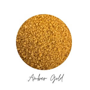 Close-up circle swatch of Amber Gold craft sand with the color name written below
