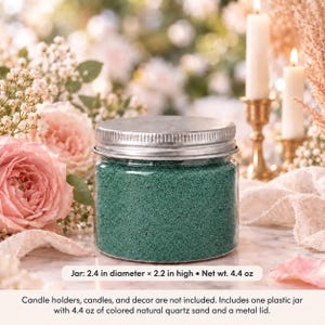 Closed clear jar of deep teal green colored quartz sand with a silver metal screw lid on a marble table, surrounded by pink roses, baby's breath, lit white candles in brass holders and cream fabric. Text: Jar: 2.4 in diameter x 2.2 in high, Net wt. 4.4 oz. Candle holders, candles, and decor are not included. Includes one plastic jar with 4.4 oz of colored natural quartz sand and a metal lid.
