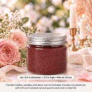 Closed clear jar of deep red colored quartz sand with a silver metal screw lid on a marble table, surrounded by pink roses, baby's breath, lit white candles in brass holders and cream fabric. Text: Jar: 2.4 in diameter x 2.2 in high, Net wt. 4.4 oz. Candle holders, candles, and decor are not included. Includes one plastic jar with 4.4 oz of colored natural quartz sand and a metal lid.