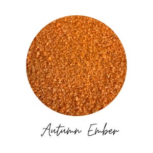 Close-up circle swatch of Autumn Ember burnt orange craft sand with the color name written below