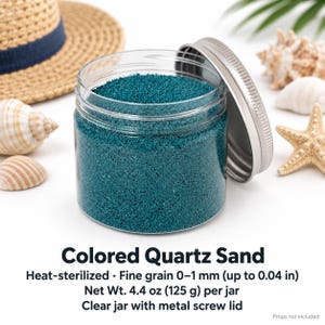 Open clear jar of Ocean Breeze colored quartz sand in a deep teal, with the silver metal lid leaning against it, next to a straw hat, seashells, a starfish and a palm leaf. Text: Colored Quartz Sand, heat-sterilized, fine grain 0-1 mm (up to 0.04 in), Net Wt. 4.4 oz (125 g) per jar, clear jar with metal screw lid, props not included.
