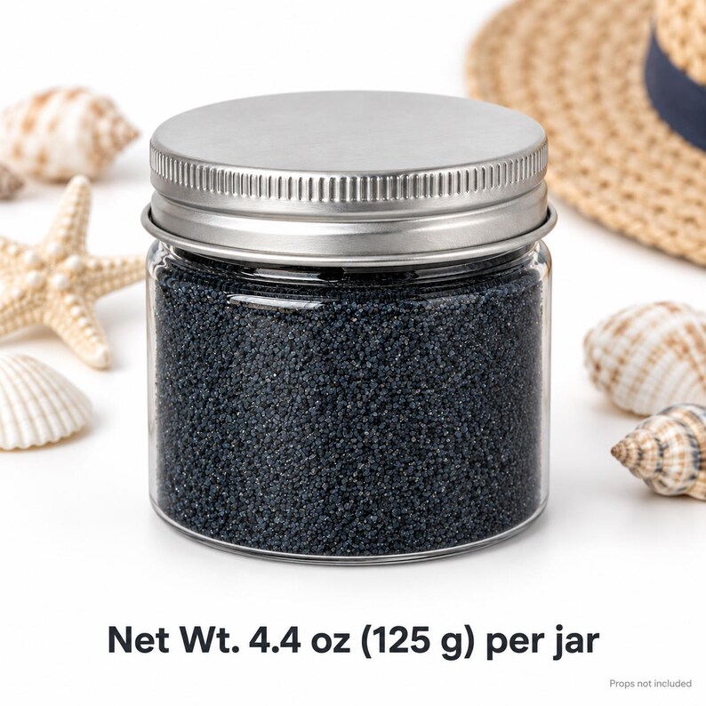 Closed clear jar of dark navy blue colored quartz sand with a silver metal screw lid, next to seashells, a starfish and a straw hat with a navy ribbon, with text: Net Wt. 4.4 oz (125 g) per jar, props not included.
