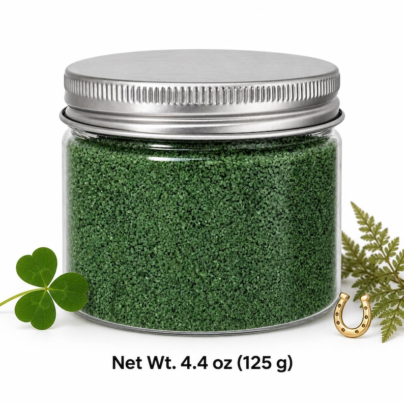 Closed clear jar of forest green colored quartz sand with a silver metal screw lid, next to a three-leaf clover, a small gold horseshoe and a fern sprig, with text: Net Wt. 4.4 oz (125 g).