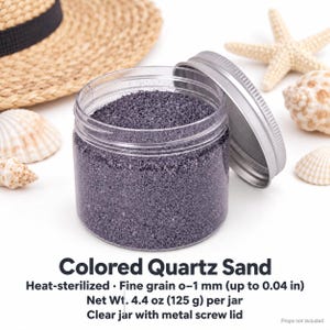 Open clear jar of Lavender Mist colored quartz sand in a soft lavender grey, with the silver metal lid leaning against it, next to a straw hat, seashells and a starfish. Text: Colored Quartz Sand, heat-sterilized, fine grain 0-1 mm (up to 0.04 in), Net Wt. 4.4 oz (125 g) per jar, clear jar with metal screw lid, props not included.