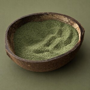 Coconut shell bowl filled with olive green craft sand on a green background