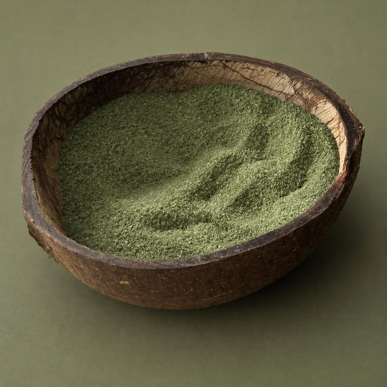 Coconut shell bowl filled with olive green craft sand on a green background