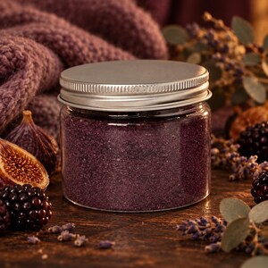 Closed clear jar of Plum Velvet colored quartz sand in a deep plum purple, with a silver metal screw lid, on a dark wooden table surrounded by fresh figs, blackberries, dried lavender, eucalyptus and a chunky plum knit blanket.