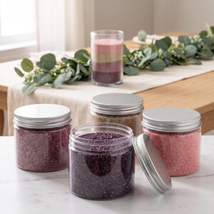 Four jars of colored quartz sand in various shades displayed on a table with a table runner
and greenery, ideal for dry terrarium styling.