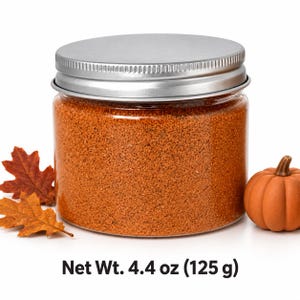 Closed clear jar of warm orange colored quartz sand with a silver metal screw lid, next to autumn oak leaves and a small orange pumpkin, with text: Net Wt. 4.4 oz (125 g).