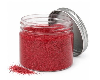 May include: A clear plastic jar filled with vibrant red granular powder, featuring a silver-coloured metal screw-top lid resting beside it. A small amount of the red powder is spilled on the surface near the base of the jar.