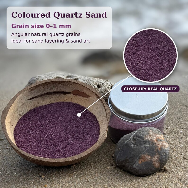 Coconut shell bowl filled with Plum Velvet colored quartz sand in a deep plum purple, next to a closed jar of the same sand with a silver metal screw lid, a grey stone and a piece of coral on a beach. A magnified circle shows the fine angular grains, labeled Close-up: Real Quartz. Text: Coloured Quartz Sand, grain size 0-1 mm, angular natural quartz grains, ideal for sand layering and sand art.