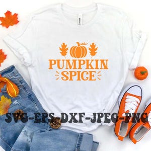Puede incluir: Camiseta blanca con un diseño naranja de calabaza y hojas. El texto "Pumpkin Spice" está escrito en naranja debajo de la calabaza.