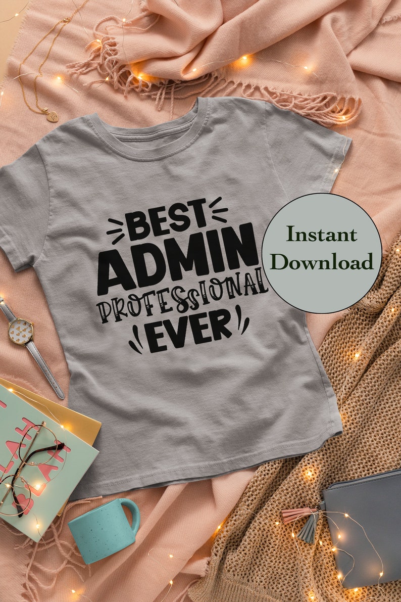 May include: A gray t-shirt with black text that reads "Best Admin Professional Ever!"  The shirt is on a pink and brown blanket with string lights.