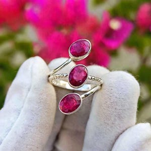 Peut inclure: Une bague en argent de style bypass ornée de trois pierres précieuses ovales d'un rouge rosé profond, disposées en spirale. L'anneau présente un motif torsadé texturé et les pierres sont serties dans des montures en argent poli et simple.