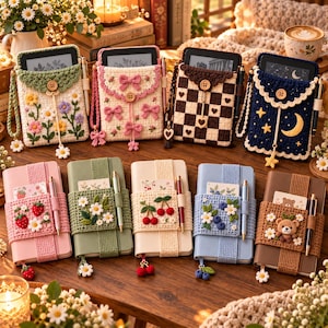 May include: A collection of four crocheted e-reader pouches featuring floral, bow, checkered, and celestial designs, alongside five notebooks wrapped in crocheted bands decorated with strawberries, daisies, cherries, blueberries, and a bear.