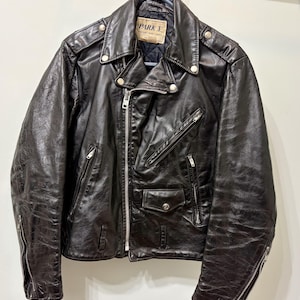 May include: A black leather motorcycle jacket featuring a silver-tone asymmetrical front zipper, multiple zippered pockets, a small snap-button flap pocket, and shoulder epaulets. The interior label reads PARK V NEW YORK PARIS LONDON.