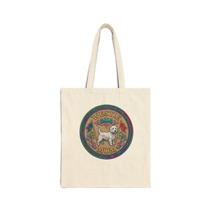 May include: A natural-colored canvas tote bag featuring a circular graphic in the center. The design displays a white West Highland White Terrier, a teal bone, two small flags, and the text "WESTIE MOM" enclosed within a colorful braided border.