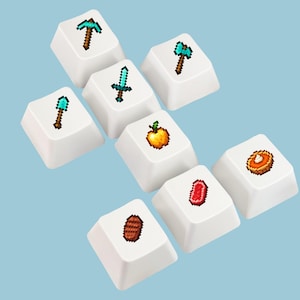 Pode incluir: Um conjunto de oito teclas brancas para teclado mecânico dispostas em forma de cruz. Cada tecla apresenta um pequeno ícone colorido em pixel art, incluindo uma picareta de diamante, um machado, uma espada, uma pá, uma maçã e carne.
