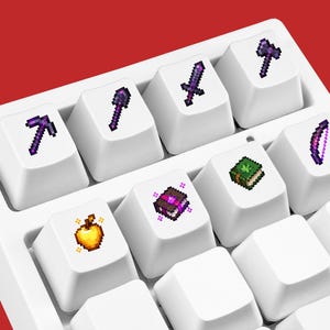 May include: A set of white mechanical keyboard keycaps featuring pixel art icons. The icons include a purple pickaxe, shovel, sword, axe, and bow, along with a golden apple, a purple enchanted book, and a green book with a leaf symbol.
