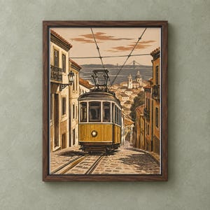 May include: A framed art print depicting a yellow tram traveling down a cobblestone street in a city. The scene features tall buildings on both sides, overhead power lines, and a distant bridge over water under a pale sky with clouds.