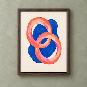 May include: A framed wall art print featuring two overlapping circular rings in shades of orange, coral, and pink. The rings are layered over a solid, irregular blue shape set against a cream-colored background, all enclosed in a dark wood frame.