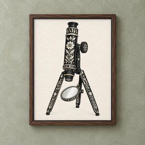 Op de afbeelding: Een ingelijste muurkunstprint met een zwart-witillustratie van een vintage microscoop. De microscoop is versierd met ingewikkelde bloemen- en bladpatronen op het hoofdgedeelte en de statiefpoten, en bevat een ronde spiegel aan de onderkant.