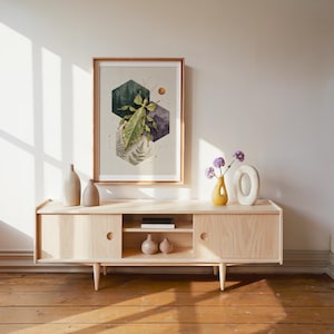 May include: A framed wall art print featuring a green leaf insect centered over three overlapping hexagons. The hexagons contain illustrations of a pine forest, a mountain range, and fern leaves. Thin copper lines form a constellation pattern.