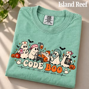 May include: A light green t-shirt featuring a graphic of ghosts dressed as medical staff with pumpkins, bats, and the text CODE BOO, RN, ER, ICU, NIGHT SHIFT. The shirt has a Comfort Colors tag showing size S, P, CH and 100% cotton material.