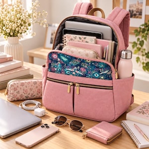 May include: A dusty pink backpack with a dark blue floral patterned front pocket, featuring gold-tone zippers, padded shoulder straps, and a side pocket holding a light pink water bottle. The interior is filled with notebooks, a tablet, and pens.