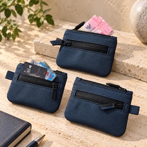 May include: Three navy blue rectangular coin pouches with a textured finish, each featuring a black zippered front pocket and a matching black zipper pull. One pouch contains pink paper currency, while another holds several credit cards.