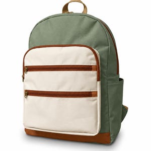 Puede incluir: Una mochila de color verde salvia con un bolsillo frontal grande de color crema que tiene dos compartimentos horizontales con cremallera. Las cremalleras y la base de la mochila tienen bordes marrones y un asa beige en la parte superior.