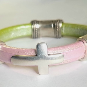 May include: A pink and green leather bracelet with a silver cross charm and crystal accents.